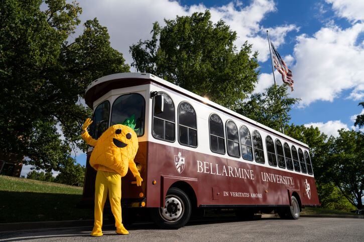 Penny the Pineapple mascot stands in front of the Bellarmine Trolley.
