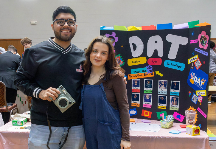 Two students standing in front of a table with a sign that says DAT