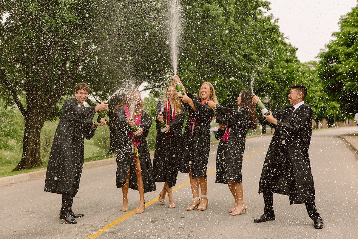 Graduates pop champagne under the arch