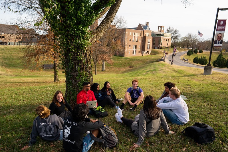 Students sit and chat around a tree on campus grounds