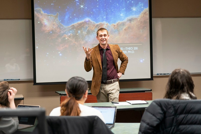 a smarmy professor presents a lecture to his theology class