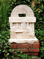 stone sculpture with arch on a brick pedestal surrounded by ivy