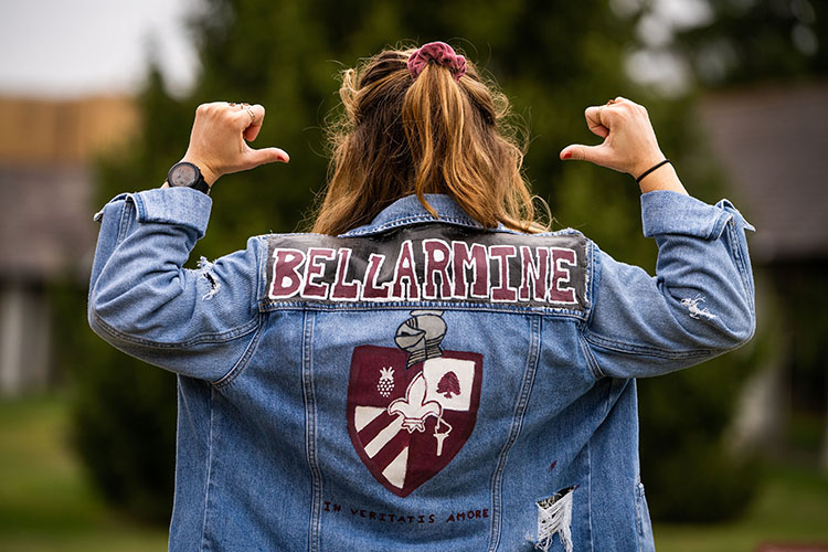 Student pointing to hand painted bellarmine on her jean jacket