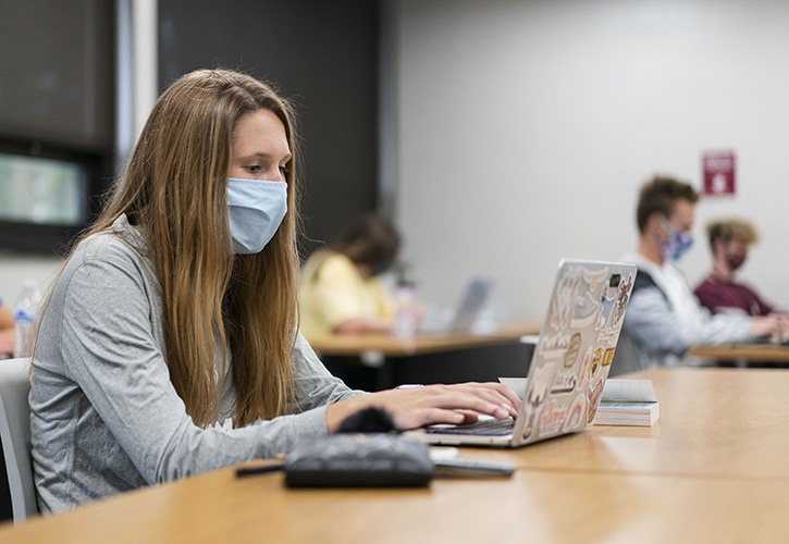 A student in class using a laptop and wearing a face mask