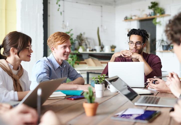 Young people around a table with laptops, talking