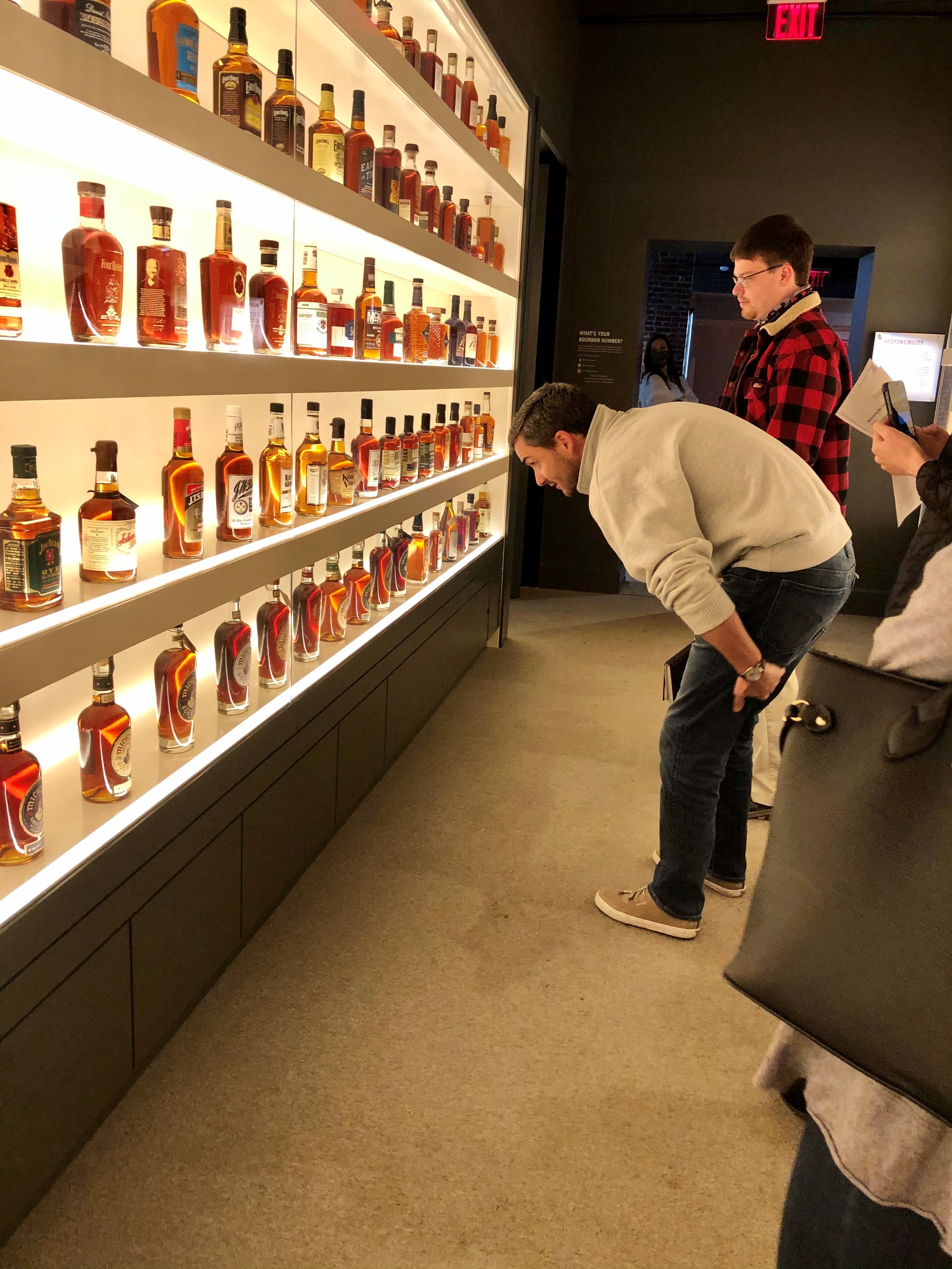 a student examines shelves displaying dozens of bottles of bourbon