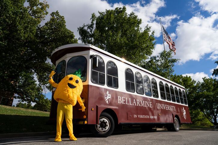 Penny the Pineapple mascot stands in front of the Bellarmine Trolley.