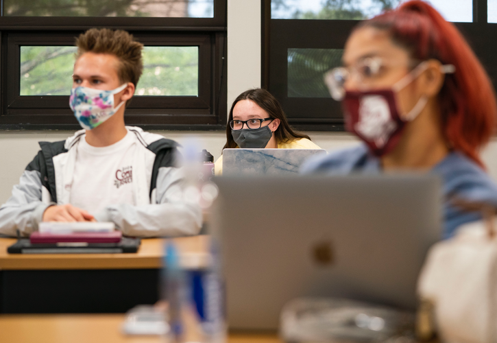 three students sitting in class, wearing masks