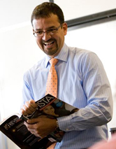 nelson lopez in a classroom, smiling while holding open a book