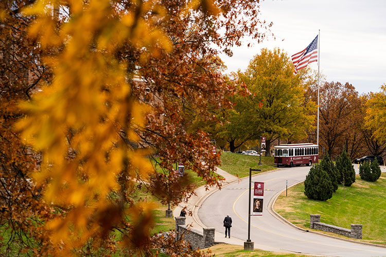 Bellarmine's campus in the fall with a trolley and American flag in the background.