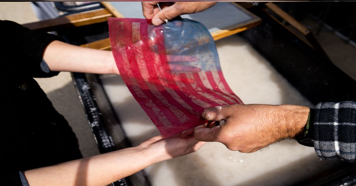 Two people hold an American flag made of paper at the Frontline Paper Workshop