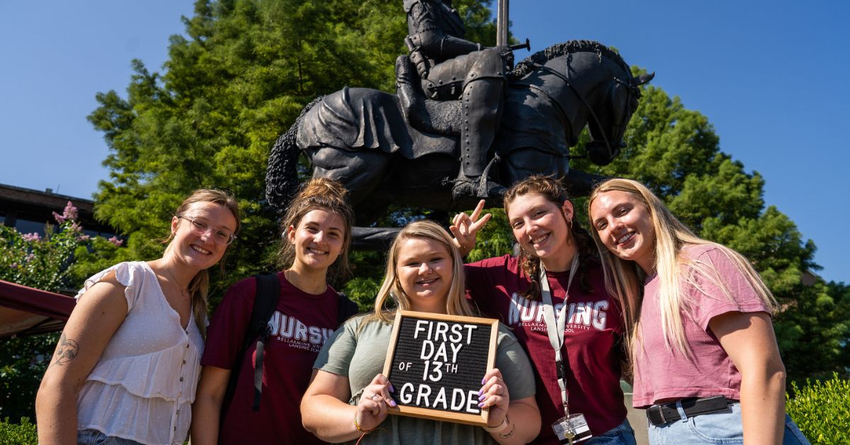 Incoming first year students hold a "First Day of 13th Grade" sign in front of the Knight statue in the Quad.
