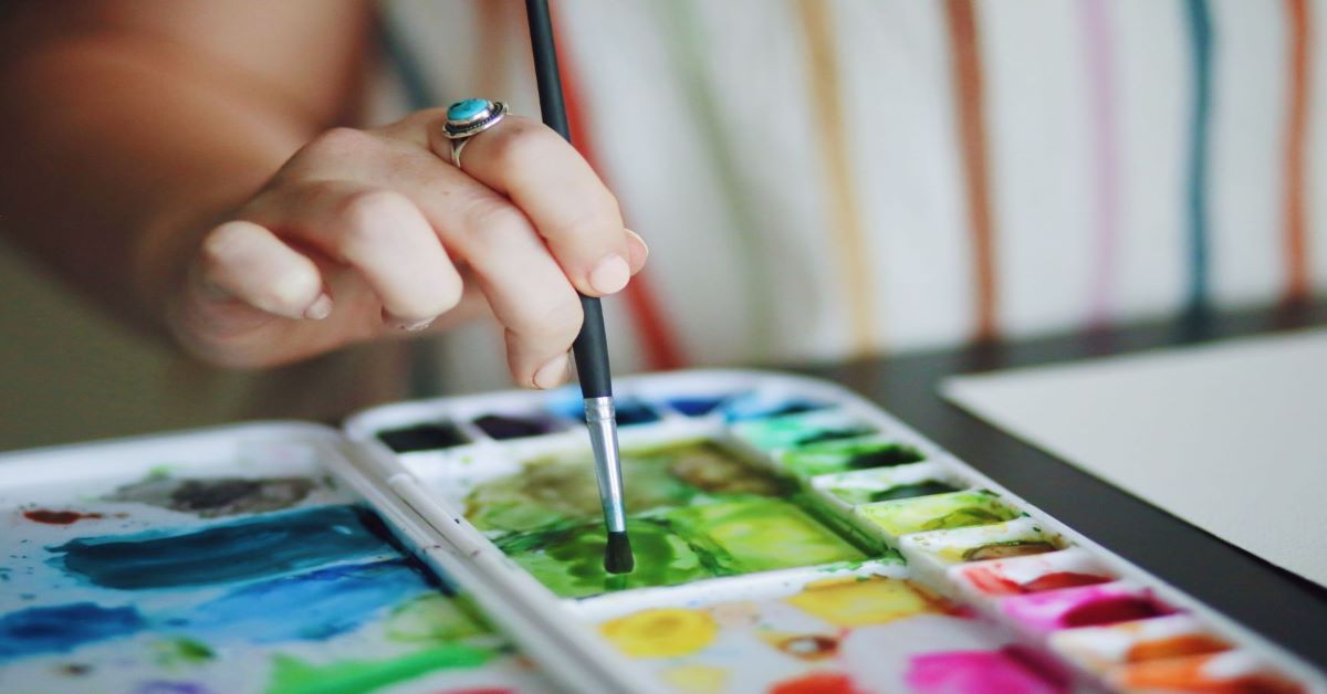 Photo of a person daubing a paintbrush into watercolors