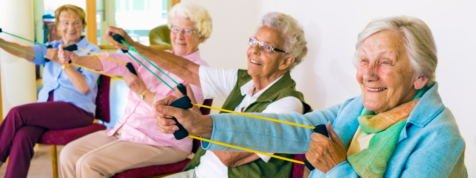 a group of senior citizens sit in a recreation room and exercise with low-impact equipment