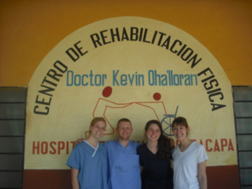 four students stand in front of a sign for a hospital in guatemala