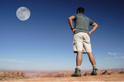 a man stands in the desert and looks at the full moon