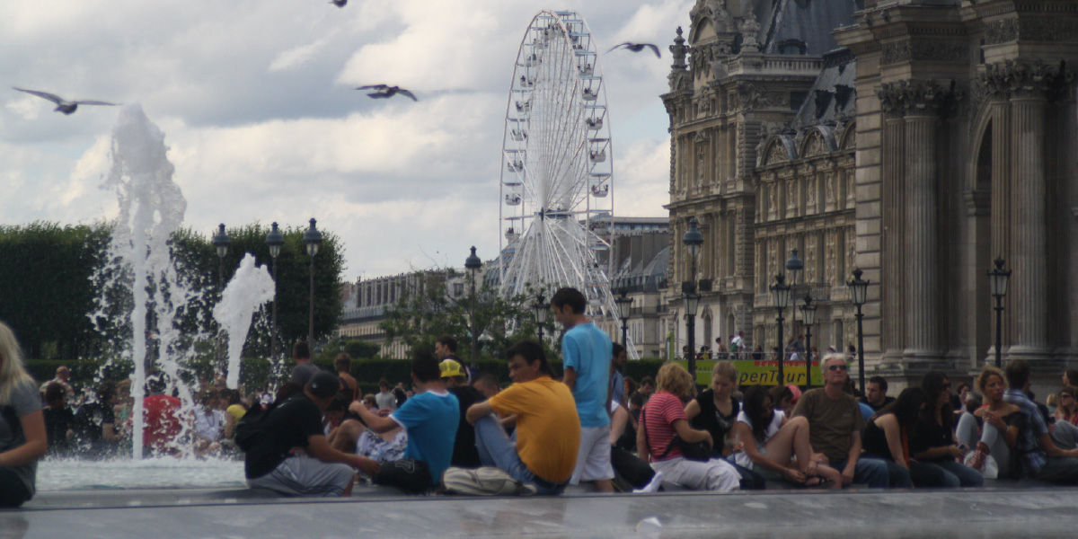 students sit in a paris pavillion with a ferris wheel in the distance